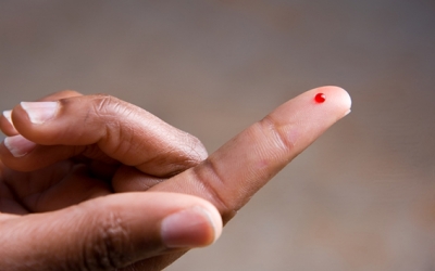 A drop of blod on a young African American woman's fingertip.  She is preparing to perform a blood sugar test.